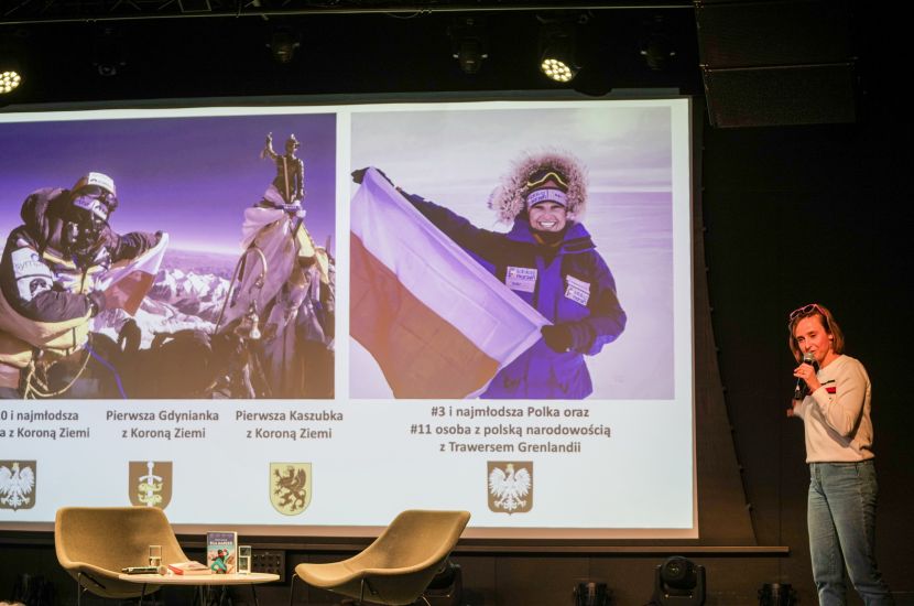 Zdjęcie przestawia Miłkę Raulin podczas spotkania autorskiego na zdjęciu widać również prezentację multimedialną przygotowaną przez autorkę