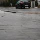 Uwaga, marznące opady deszczu! Na zdjęciu wykonanym z perspektywy żaby widać śliską nawierzchnię ulicy i stojący w oddali, na poboczu, samochód.