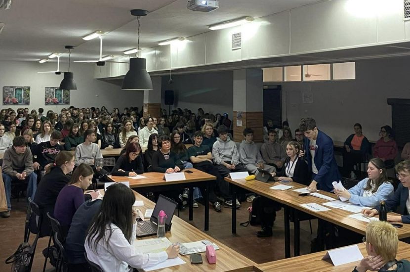 II LO z Konina w projekcie LiveON. Na zdjęciu widać grupę młodych osób siedzących wokół stołu i w przestrzeni dla widowni.