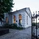 Architektoniczna perełka odzyska blask. Na zdjęciu zrobionym o zmierzchu widać otwartą bramę wjazdową, za nią w tle jest synagoga z rozświetlonymi oknami. Z lewej strony fragment budynku zasłania drzewo.