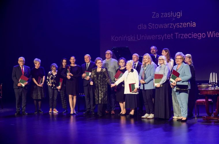 Są też inne światy… 20-lecie Konińskiego Uniwersytetu Trzeciego Wieku Na zdjęciu widać ludzi stojących na scenie, w granatowej poświacie, laureatów wyróżnień  przyznanych przez KUTW.