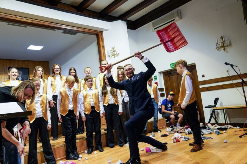 Święto muzyki chóralnej w PSM. Na scenie widać chór i dyrygenta z plastikową łopatą podniesioną do góry - elementem choreografii.
