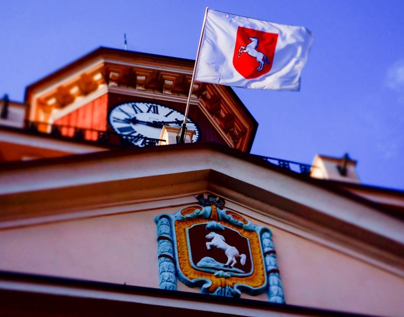 Radni z Poznania za atomem dla Konina. Na zdjęciu jest widoczna wieża ratusza i fragment górnej części budynku z herbem miasta i miejską flagą powiewającą na wietrze.