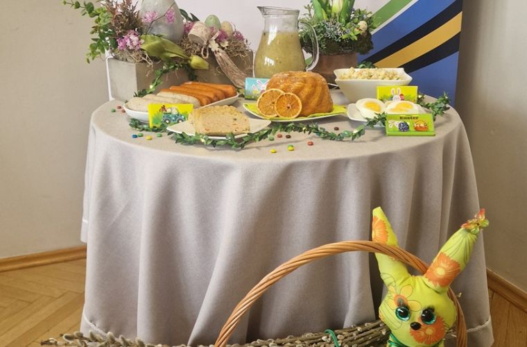 Wielkanocna pomoc dla potrzebujących. Na zdjęciu widać stół zastawiony wielkanocnymi potrawami, za nim jest baner MOPR, przed koszyk z króliczkiem.