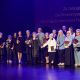 Są też inne światy… 20-lecie Konińskiego Uniwersytetu Trzeciego Wieku Na zdjęciu widać ludzi stojących na scenie, w granatowej poświacie, laureatów wyróżnień  przyznanych przez KUTW.