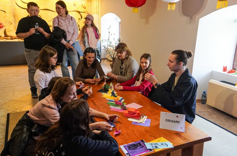 Na zdjęciu widoczna grupa ludzi przy stole do origami podczas Japońskiego pikniku w Muzeum