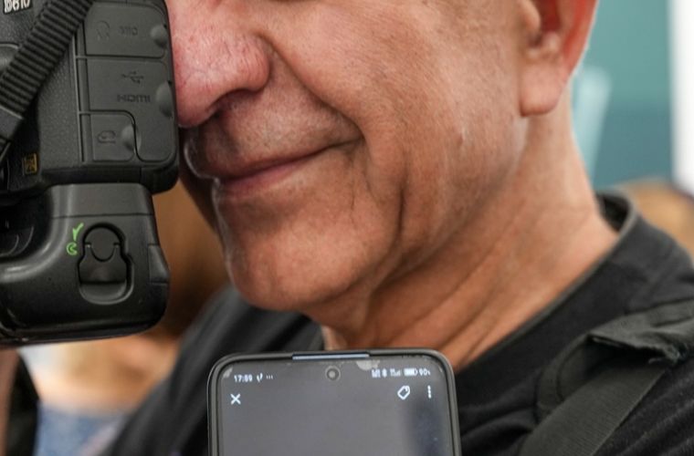 Tadeusz Topolski ze złotym medalem. Na zdjęciu widać zbliżenie na twarz Topolskiego, ma aparat przy oku, przed nim na telefonie wyświetla się medal.