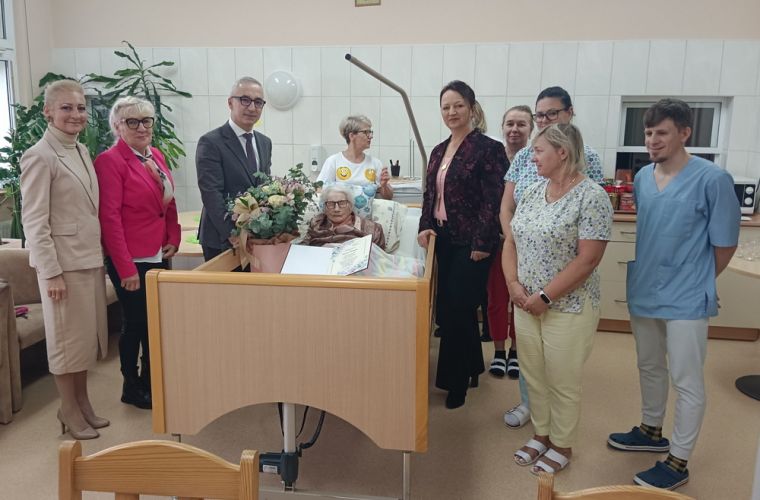 102 lata ukończyła pani Janina Wałęsa. Na zdjęciu widać jubilatkę leżącą na łożku szpitalnym, obok niej z-ca prezydenta i kierownik USC oraz personel i bliscy jubilatki.