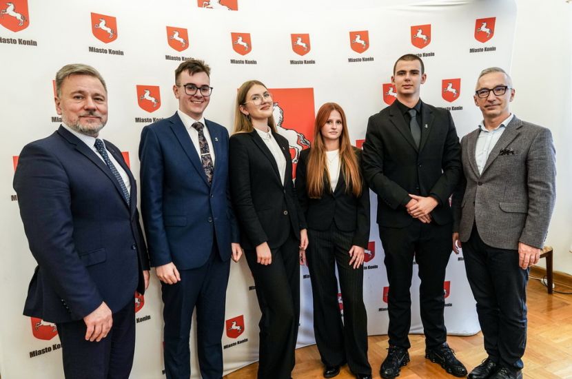 Nowa kadencja Młodzieżowej Rady Miasta Konina. Na zdjęciu prezydent Piotr Korytkowski i zastępca Witold Nowak wraz prezydium Młodzieżowej Rady stoją na tle banera z herbem miasta.