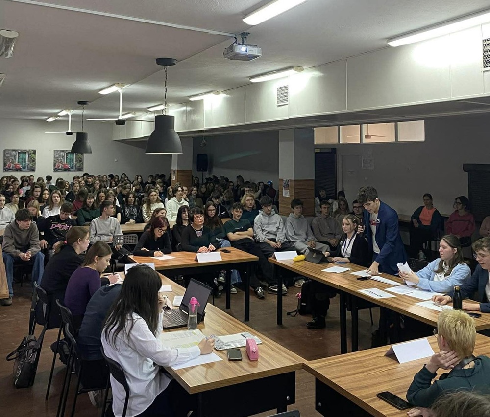 II LO z Konina w projekcie LiveON. Na zdjęciu widać grupę młodych osób siedzących wokół stołu i w przestrzeni dla widowni.