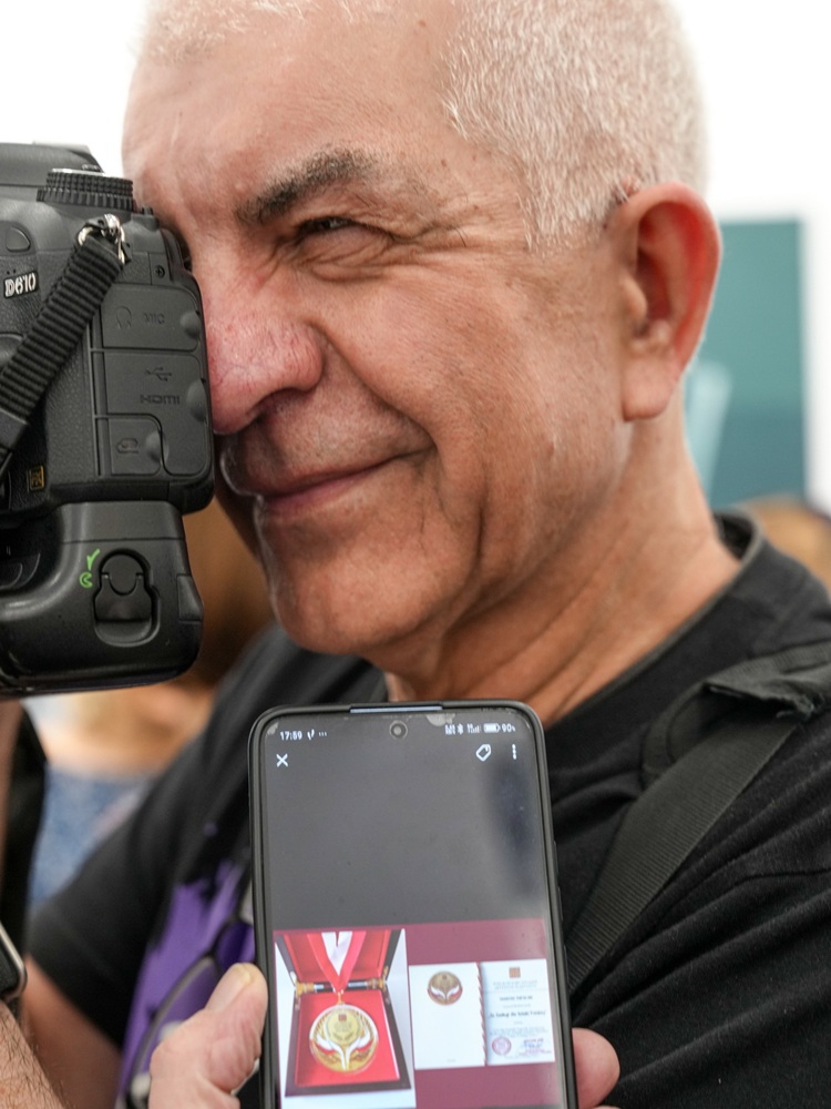 Tadeusz Topolski ze złotym medalem. Na zdjęciu widać zbliżenie na twarz Topolskiego, ma aparat przy oku, przed nim na telefonie wyświetla się medal.