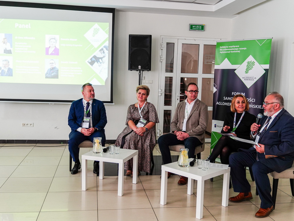 Współpraca kluczem do przyszłości. I Forum Samorządności Aglomeracji Konińskiej. Na zdjęciu widać pięcioro prelegentów podczas dyskusji, siedzących w półkolu, na tle bannera Aglomeracji Konińskiej