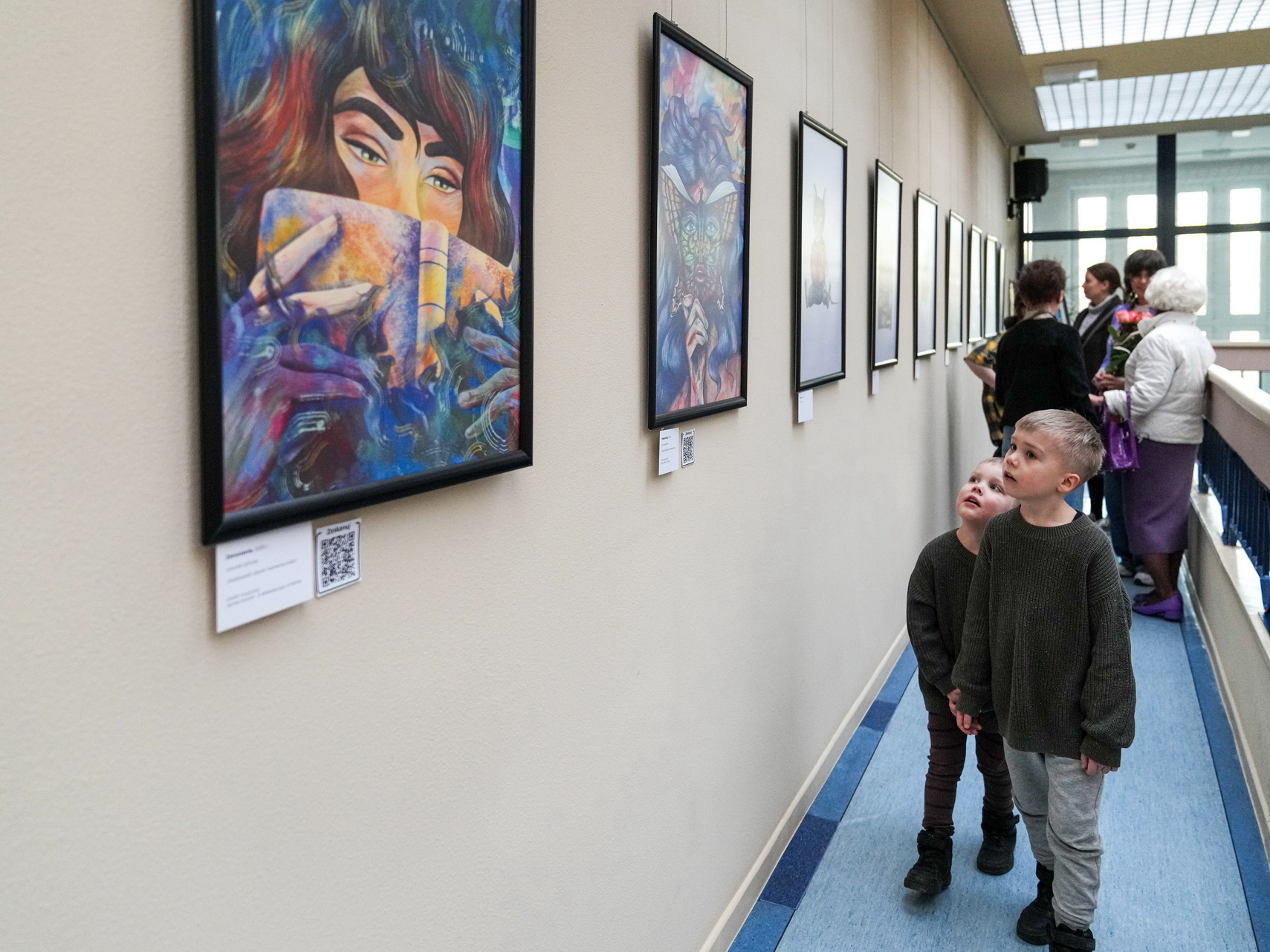 Zdjęcie przedstawia dwóch chłopców oglądających prace na wystawie Magdaleny Jakubowskiej w bibliotece
