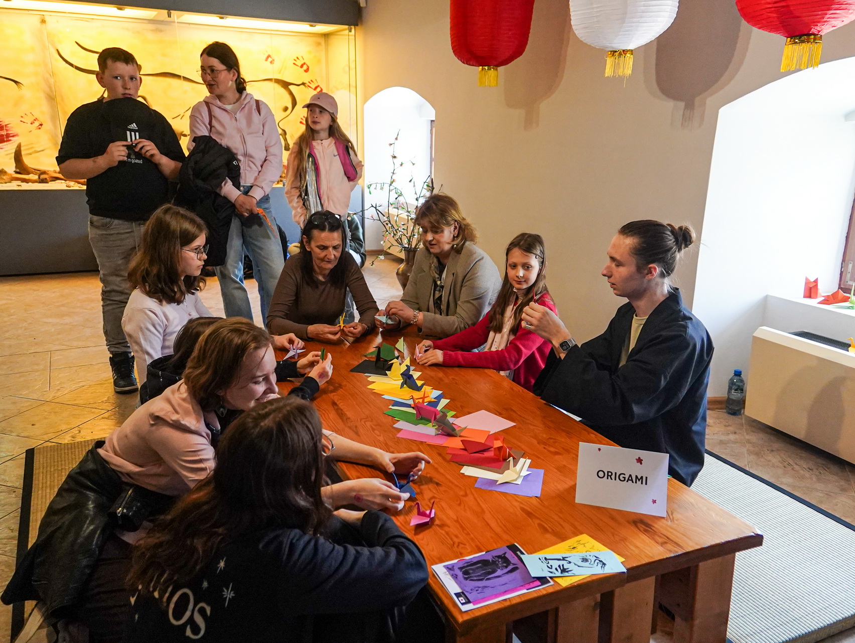 Na zdjęciu widoczna grupa ludzi przy stole do origami podczas Japońskiego pikniku w Muzeum